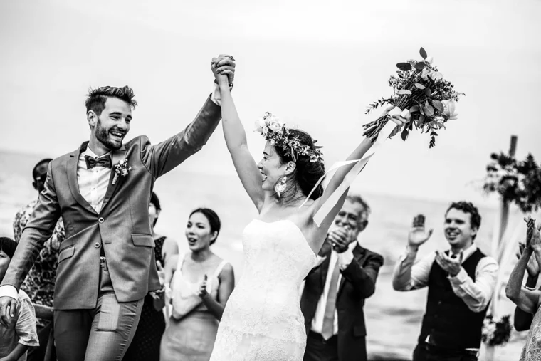 Newlyweds raising their arms by the sea