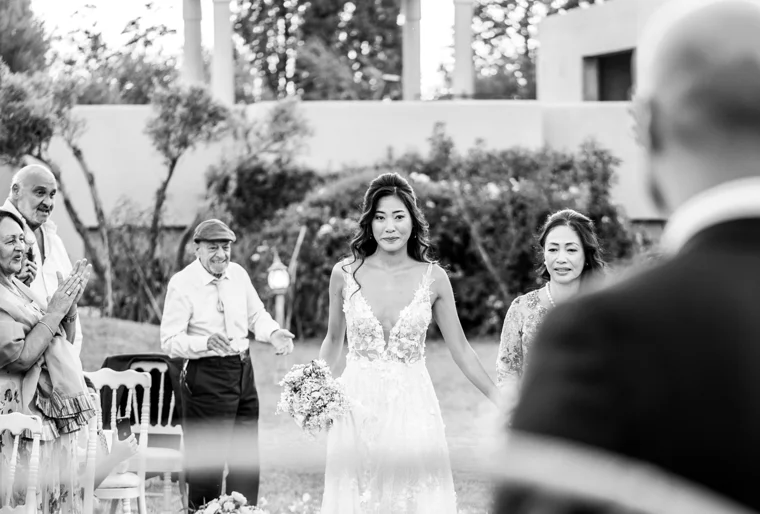 Black-and-white wedding photograph of a bride arriving at the garden ceremony